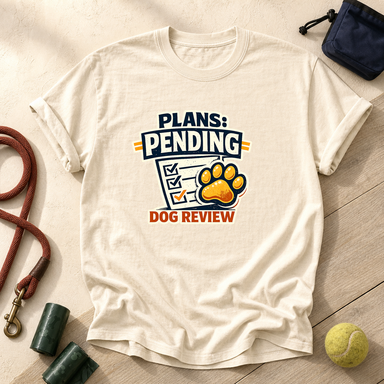 Ivory Comfort Colors T-shirt printed with Plans Pending Dog Review, a checklist and a friendly paw-print stamp, surrounded by dog-walk props.